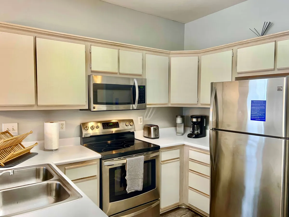 The image showcases a contemporary kitchen with a stainless steel refrigerator, a modern stove, sink, coffee maker, and a drying rack for dishes. The countertops are spotless, and the overall design emphasizes both style and functionality, hinting at high-end appliances and inviting warm gatherings.