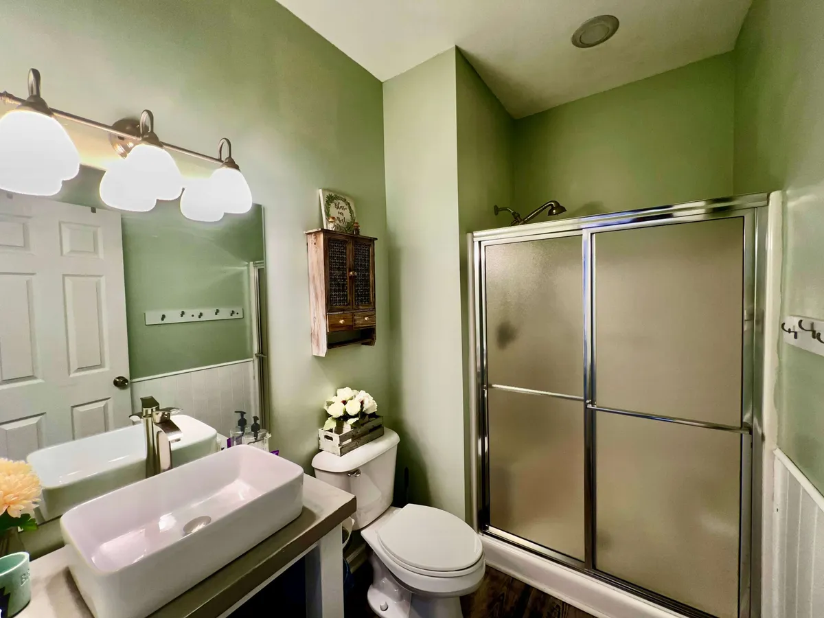 A modern bathroom with a sleek vanity and sink, a glass-enclosed shower, a decorative wall shelf, and a mirror reflecting ample light. The space is adorned with subtle, spa-inspired accents, evoking a soothing and refreshing mood.