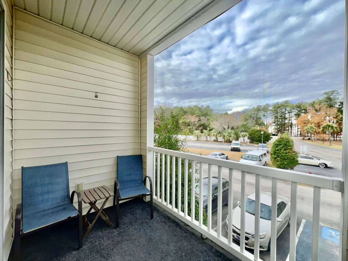 Two blue chairs and a small wooden table are set up on a balcony overlooking a quiet street and lush greenery. The setting is relaxed, ideal for unwinding after a round of golf or enjoying a morning coffee with a view of the outdoors.