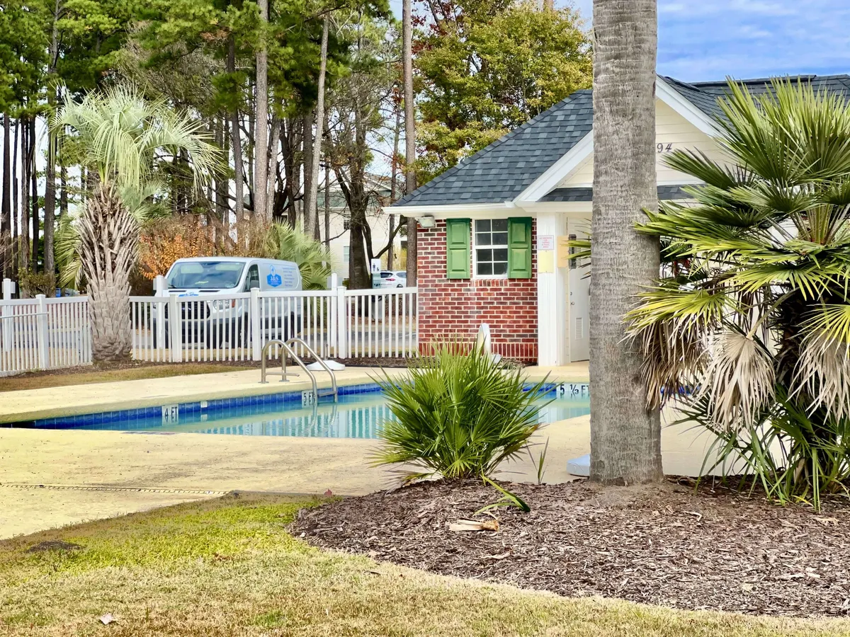 Another view of the exterior pool area, showcasing the sparkling swimming pool, a brick building, and palm trees within a secure, fenced setting. The tranquil atmosphere is ideal for unwinding after a day of shopping or entertainment.