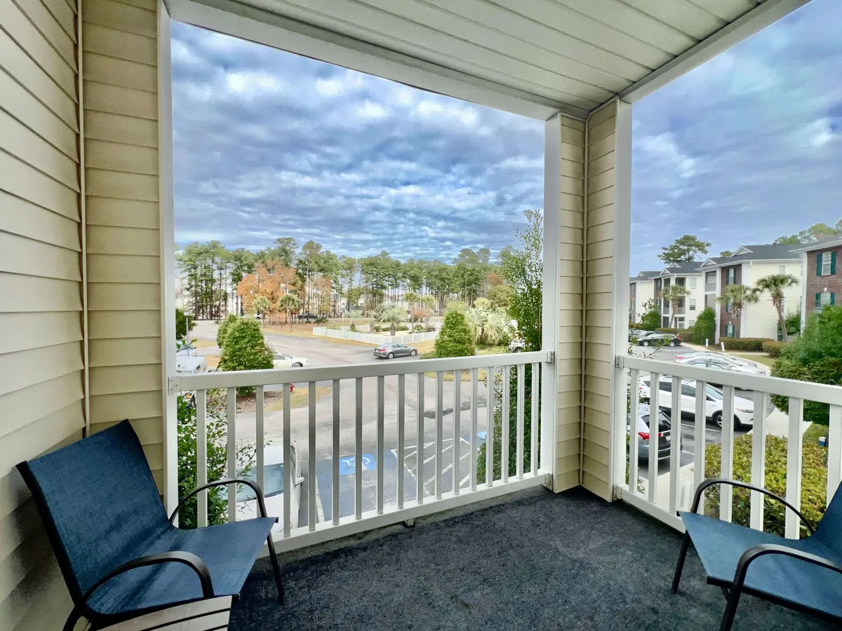 This image captures a private balcony with blue chairs set against a backdrop of trees and residential buildings. The balcony railing offers a clear view, and the overall scene radiates a peaceful, inviting atmosphere perfect for savoring coffee in the morning or unwinding at sunset.
