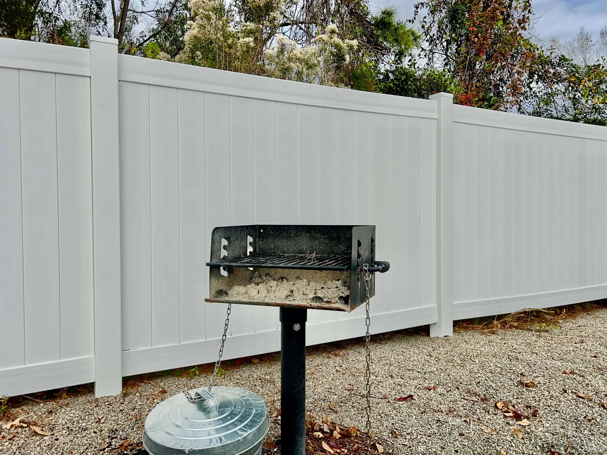 The image features a grill set on gravel ground, framed by a white fence. The relaxed layout evokes casual outdoor gatherings—ideal for sharing meals and making memories with friends and neighbors.