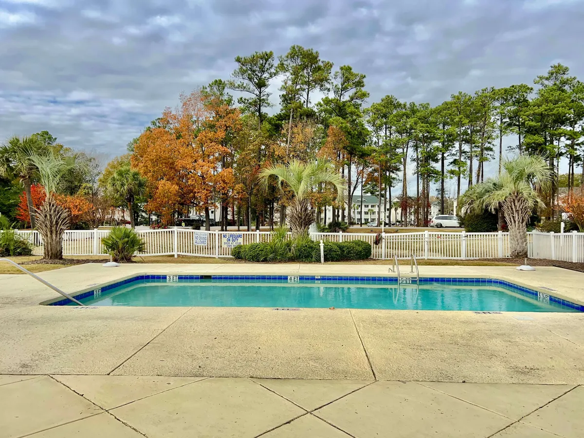 This exterior image captures a serene swimming pool surrounded by trees and a fence, with the soft glow of sunset creating a peaceful and inviting atmosphere. The area is ideal for relaxing by the water, enjoying quiet mornings, or hosting intimate gatherings beneath the trees.